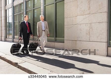 Businessmen rolling luggage outdoors View Large Photo Image Stock Photography - Businessmen rolling luggage outdoors. Fotosearch