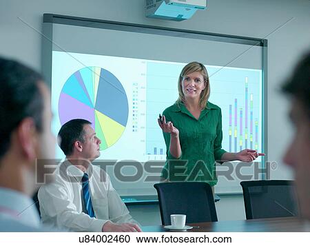 Stock Image - Businesswoman explaining to colleagues in conference room using smart board. Fotosearch
