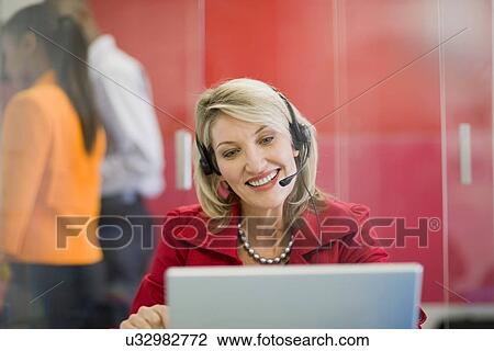 Stock Image - Businesswoman on headset using laptop. Fotosearch