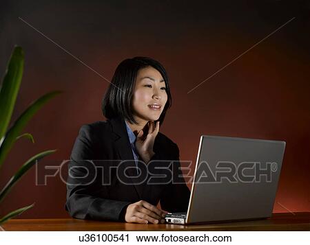 Stock Image - Businesswoman using laptop at desk. Fotosearch