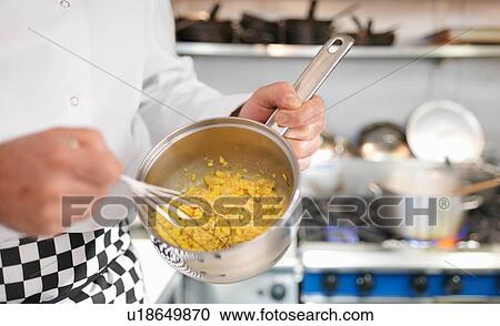 Stock Image - Chef in restaurant whisking scrambled egg and Scottish smoked salmon in pan. Fotosearch