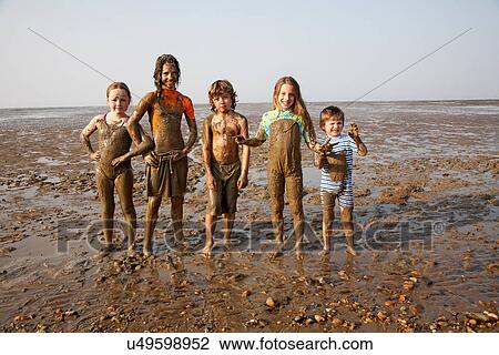 Stock Image - Children covered in mud on rocky beach. Fotosearch