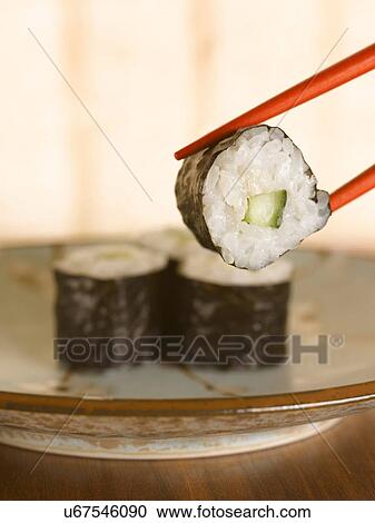 Stock Image - Close up of chopsticks holding sushi. Fotosearch