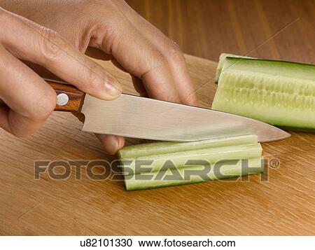 Stock Image - Close up of woman chopping cucumber. Fotosearch