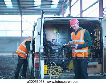 Stock Image - Construction worker checking clipboard in back of van on building site. Fotosearch