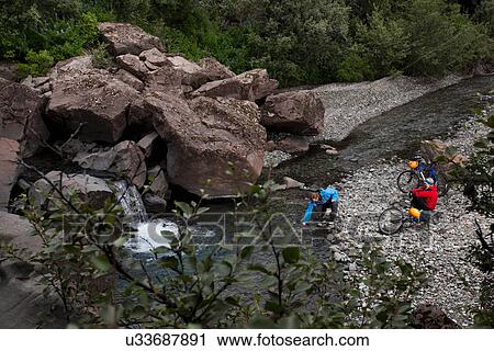 Stock Image - Couple crossing creek with bicycles. Fotosearch