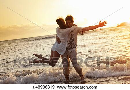 Stock Photo - Couple playing in waves at beach. Fotosearch