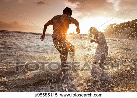 Couple playing in waves at beach View Large Photo Image Stock Photography - Couple playing in waves at beach. Fotosearch
