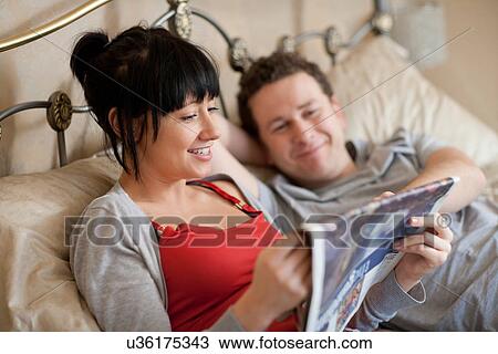 Stock Image - Couple reading newspaper in bed. Fotosearch