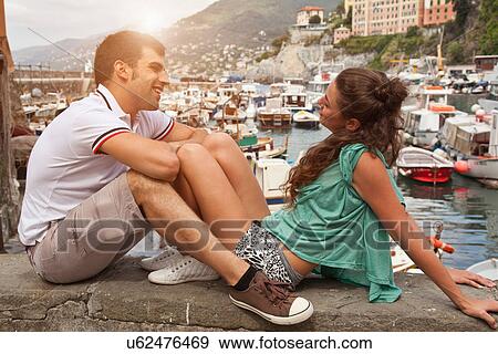 Stock Photo - Couple relaxing on stone wall by pier. Fotosearch