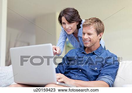 Stock Image - Couple using laptop together on couch. Fotosearch