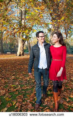 Stock Image - Couple walking in park among fall leaves. Fotosearch