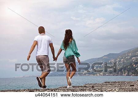 Stock Image - Couple walking on rocky beach. Fotosearch