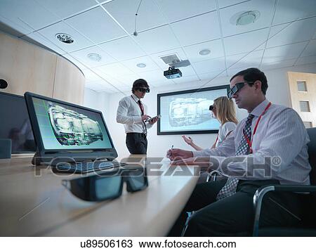 Stock Image - Engineers and apprentice in meeting room wearing 3D glasses to look at 3D screens. Fotosearch