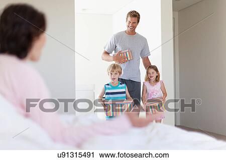 Stock Image - Family bringing mother presents in bed. Fotosearch