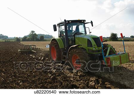 Stock Image - Farmer driving tractor through fields. Fotosearch