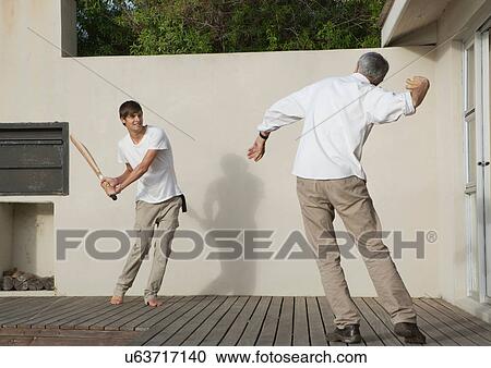 Stock Image - Father and son playing cricket on patio. Fotosearch