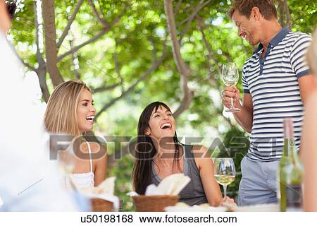 Stock Photo - Friends having wine at table outdoors. Fotosearch