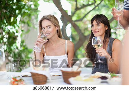 Stock Photo - Friends having wine at table outdoors. Fotosearch
