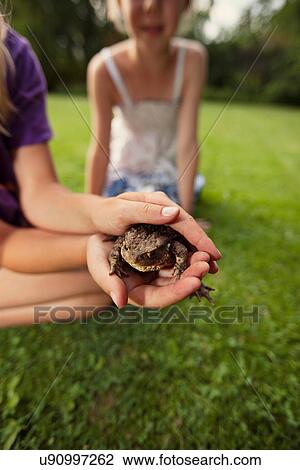 Stock Image - Girl holding frog in backyard. Fotosearch