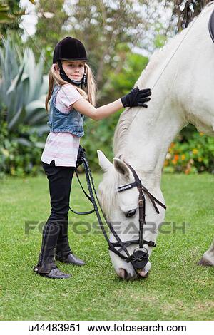 Girl petting grazing horse in park View Large Photo Image Stock Image - Girl petting grazing horse in park. Fotosearch