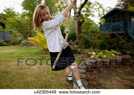 Stock Photo - Girl playing on rope swing in backyard. Fotosearch