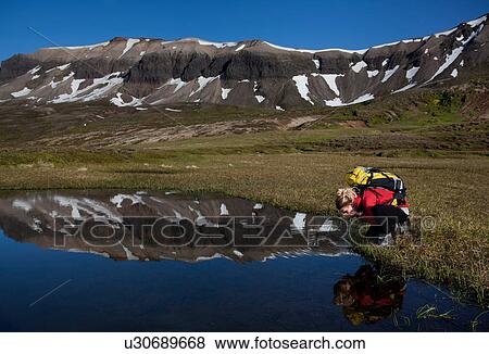 Stock Photo - Hiker admiring reflection in still pond. Fotosearch