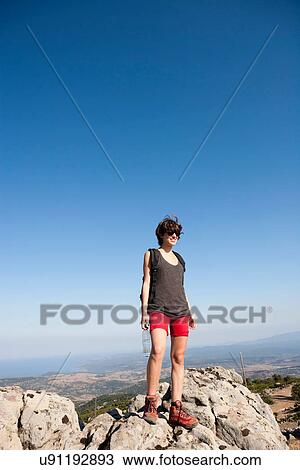 Stock Image - Hiker standing on rocks on hill. Fotosearch
