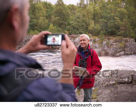 Hiker taking photograph on smartphone by flowing Scottish river View Large Photo Image Stock Photo - Hiker taking photograph on smartphone by flowing Scottish river. Fotosearch