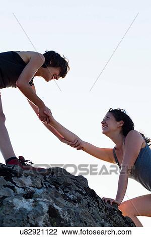 Stock Image - Hikers helping each other climb rock. Fotosearch