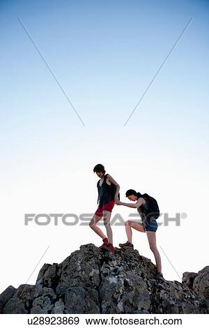 Stock Photo - Hikers helping each other climb rock. Fotosearch