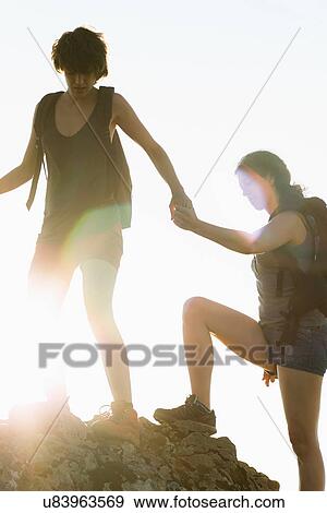Stock Photo - Hikers helping each other climb rock. Fotosearch