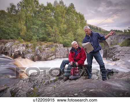 Stock Photography - Hikers reading map by flowing Scottish river. Fotosearch