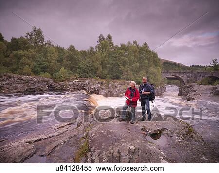 Stock Photography - Hikers standing on rocks by flowing Scottish river. Fotosearch