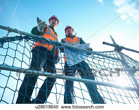 Low angle view through scaffolding of builders holding plans on factory roof View Large Photo Image Stock Photography - Low angle view through scaffolding of builders holding plans on factory roof. Fotosearch