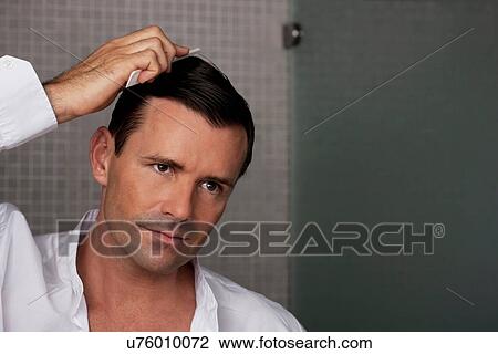 Stock Image - Man combing his hair in bathroom. Fotosearch
