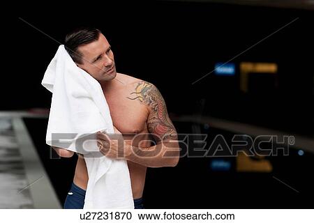Stock Image - Man drying off by pool at night. Fotosearch