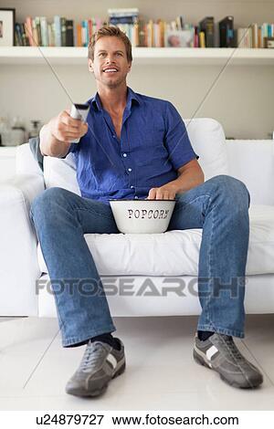 Stock Photo - Man eating popcorn and watching TV. Fotosearch
