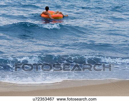 Stock Photo - Man floating in inner tube in ocean. Fotosearch