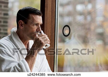 Stock Photography - Man in bathrobe drinking water by window. Fotosearch