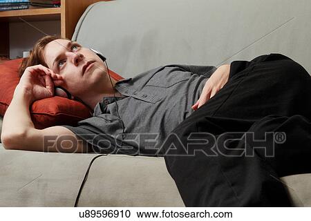 Man listening to headphones on couch View Large Photo Image Stock Image - Man listening to headphones on couch. Fotosearch