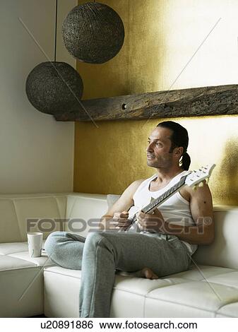 Man playing guitar on couch View Large Photo Image Stock Photograph - Man playing guitar on couch. Fotosearch