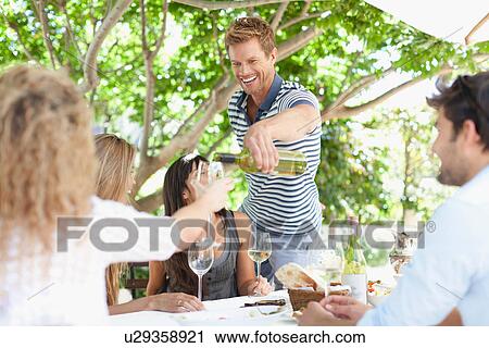 Man pouring wine for friends at table View Large Photo Image Stock Image - Man pouring wine for friends at table. Fotosearch