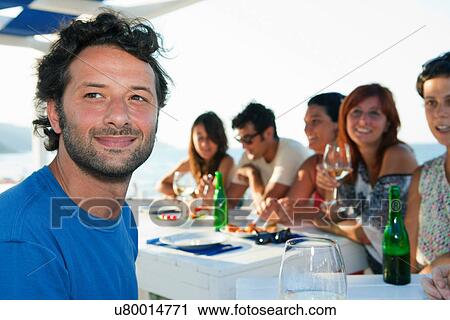 Man smiling at table with friends View Large Photo Image Stock Image - Man smiling at table with friends. Fotosearch