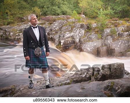 Stock Image - Man standing by river in Prince Charlie outfit with Douglas Modern Tartan. Fotosearch