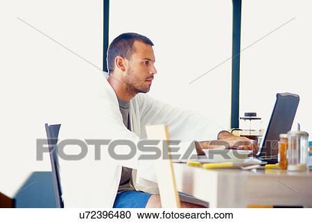 Stock Image - Man using laptop at breakfast table. Fotosearch