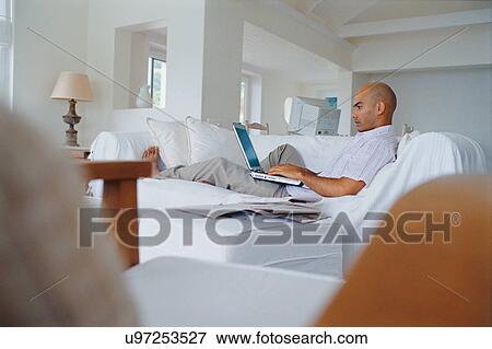 Man using laptop on couch View Large Photo Image Stock Photo - Man using laptop on couch. Fotosearch