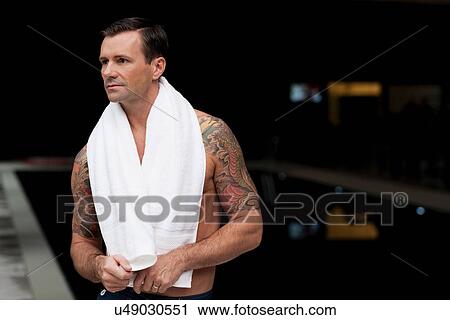 Stock Image - Man wearing towel by pool at night. Fotosearch
