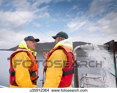Picture - Men working in Scottish salmon farm on loch. Fotosearch
