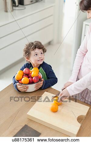 Stock Image - Mother and son slicing fruit in kitchen. Fotosearch